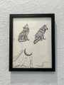 A black-framed artwork on a white wall depicting abstract figures and a crescent moon drawn in simple line work on a cream background.