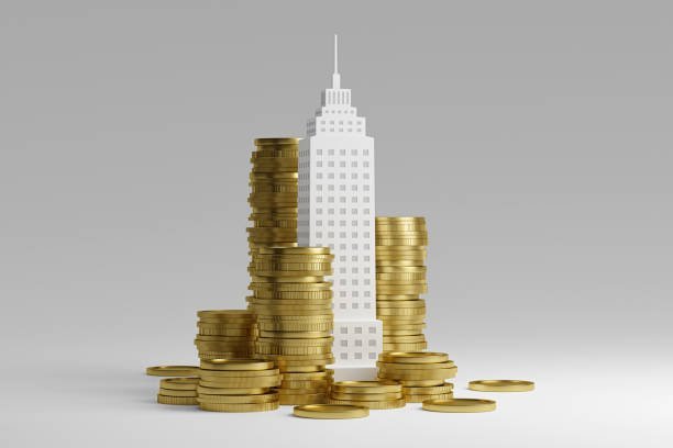 A 3D illustration of a white skyscraper model surrounded by several tall stacks and piles of gold coins against a plain gray background.