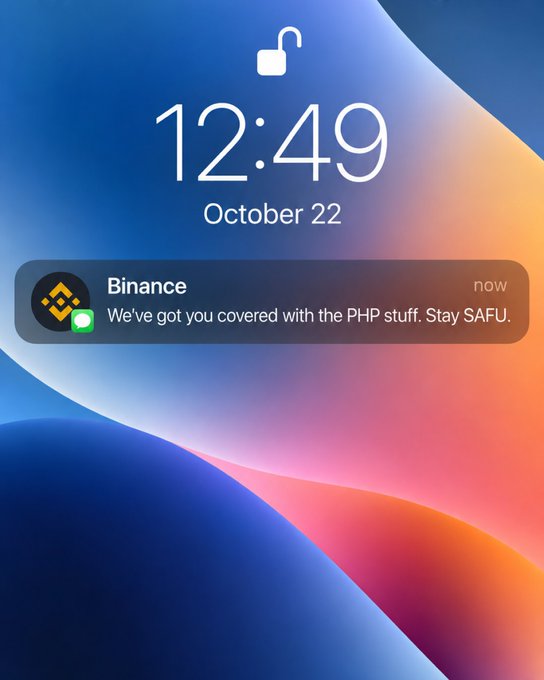 An iPhone lock screen displays the time 12:49 and date October 22, with an unlocked notification from Binance saying, “We’ve got you covered with the PHP stuff. Stay SAFU.”