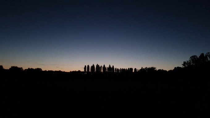 A twilight sky transitions from deep blue to a soft orange glow at the horizon, with silhouetted trees forming a dark treeline below. The serene sunset complements the post's reflective tone about new beginnings in October, capturing a quiet moment before nightfall.