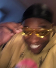 A man wearing yellow sunglasses smiles broadly while holding the glasses, radiating triumphant excitement. The image captures the thrill and smug satisfaction of outpacing a competitor in a crypto trade, perfectly mirroring the post's celebration of buying a token at half the market cap before an onchain rival.