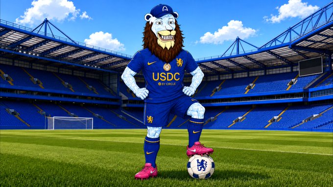 A blue lion mascot wearing a Chelsea-style soccer uniform with 'USDC BY CIRCLE' on the jersey stands on a soccer field with a football at its feet, set in a large blue stadium.