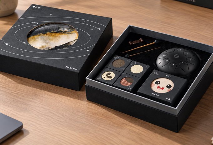 A photograph of an open NEXCOM branded gift box containing various small black electronic accessories, cables, and components with planet/solar system themed packaging.