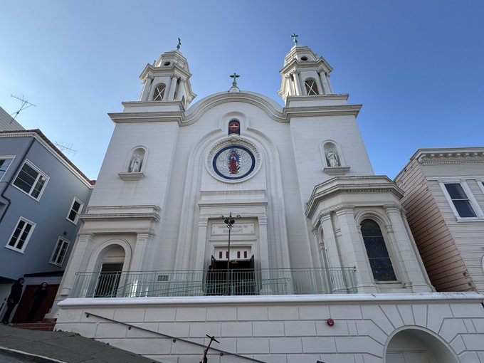 A grand white church with twin bell towers and crosses, featuring a central circular mosaic and statues in niches, stands prominently against a clear blue sky. The image's themes of strength and pride in following one's passion contrast with the traditional religious setting, suggesting the "haters" message is unrelated to the serene ecclesiastical scene depicted.