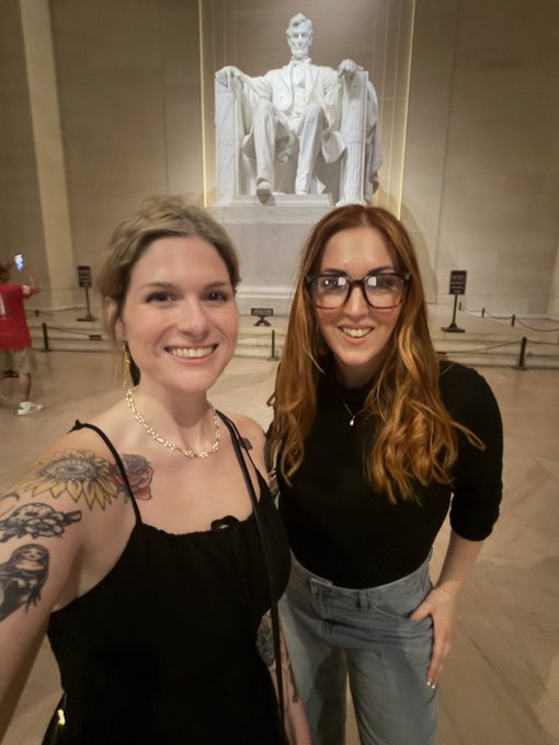 Two women smiling at the camera in front of the seated Abraham Lincoln statue inside the Lincoln Memorial.