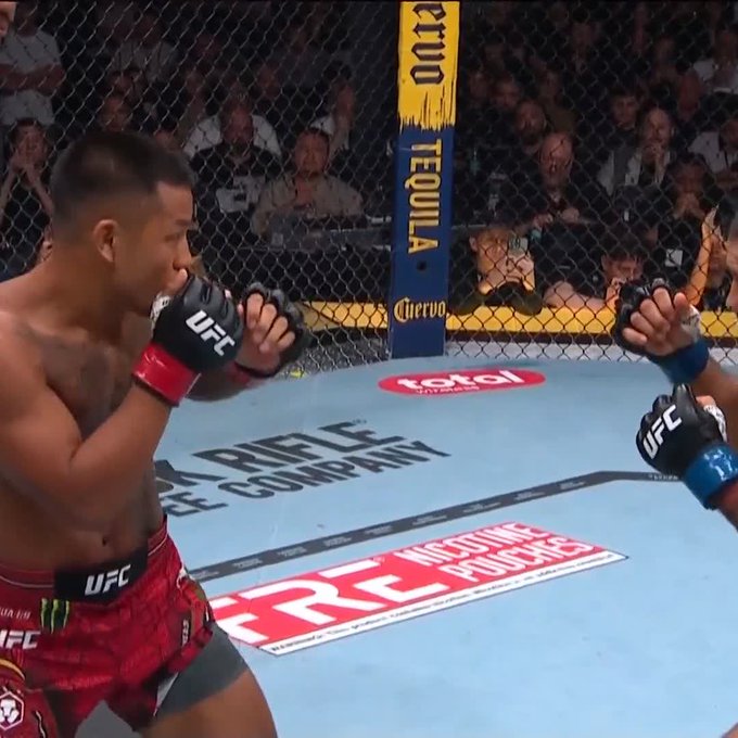Two UFC fighters face off inside the octagon at #UFC331, with one fighter in red shorts throwing a punch while his opponent blocks with a blue-taped UFC glove, surrounded by sponsorship banners for Cuervo Tequila, Total Wireless, and "Hoodie" Productions.
