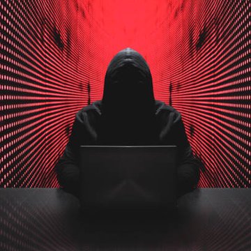 A hooded figure sitting at a laptop in a dark setting, illuminated by dramatic red light radiating in linear patterns from the background.