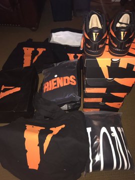 A collection of Vlone x Nike Air Force 1 sneakers, branded apparel (including a "FRIENDS" shirt), and matching orange and black packaging is laid out on a carpet. The caption "Bitcoin to the hood" emphasizes the exclusivity and streetwear value of this Vlone x Nike collaboration.