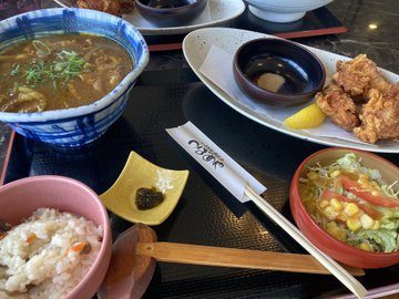 The image shows a dining table with various dishes of food, including bowls filled with different types of food such as rice, soup, salad, and meat. There are also chopsticks placed next to some of the dishes. The table appears to be set for a meal, possibly in an Asian restaurant or at home.