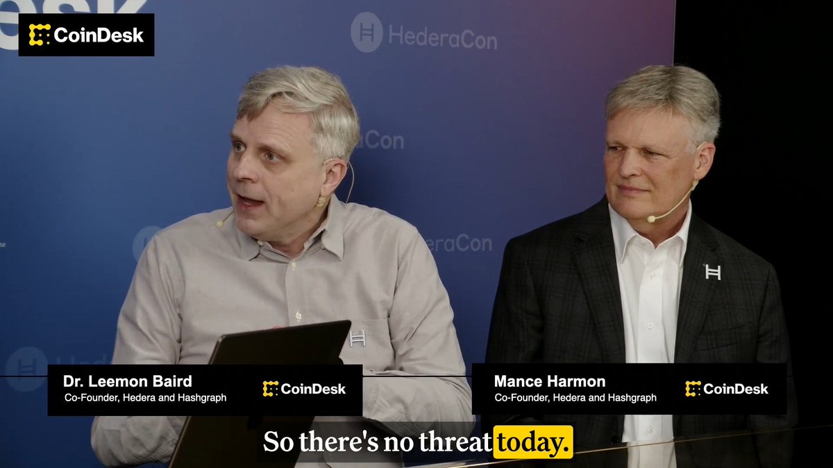 Two men identified as Dr. Leemon Baird and Mance Harmon, Co-Founders of Hedera and Hashgraph, appear at HederaCon in a CoinDesk interview, with a caption reading "So there's no threat today." Baird is speaking while wearing a headset microphone, relating to the discussion about Hedera's preparedness for "Q-day"—the anticipated arrival of quantum computing threats to current cryptography.