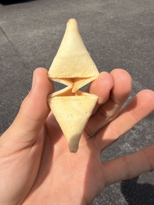 A hand holds a fortune cookie that has cracked open into two triangular halves resembling Ethereum's iconic diamond logo, tying into the post's claim that Panda Express serves ETH-shaped cookies with the ticker $ETH.