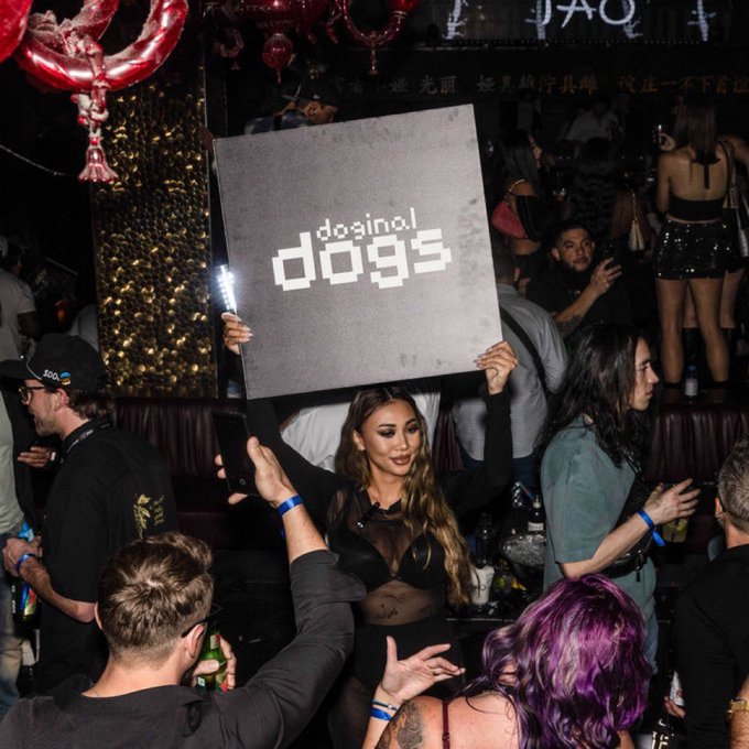 A nightclub scene at a venue called "dgsinos dog95" (or similar), showing a woman in the center holding up a large black sign with the venue's logo while surrounded by partygoers.
