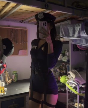 A mirror selfie of a person wearing a police officer cosplay outfit, including a hat and form-fitting navy dress with badge and utility belt, standing in a room.