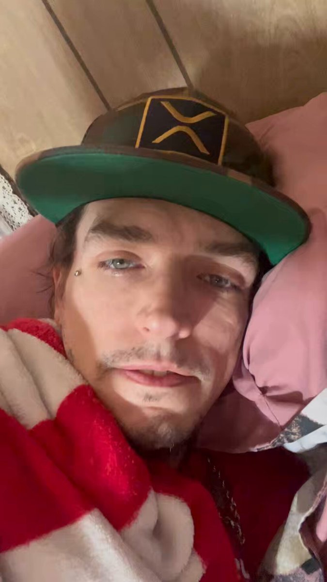 The image features a man wearing a green baseball cap with an "X" logo, lying down on his bed with a red and white striped blanket wrapped around him. The caption reads "You guys enjoying the RESET yet". This suggests that the person in the photo is likely taking a break or resting after a long day, possibly during a game of resets.

The man's face can be seen clearly against this background, with his eyes looking directly at the camera. His facial expression and body language convey a sense of relaxation and enjoyment as he rests on his bed.