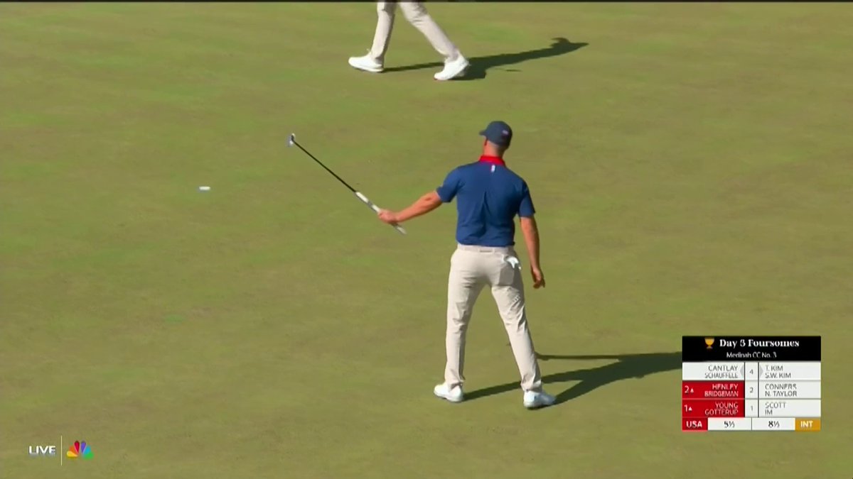 A golfer in a blue USA team shirt and white pants walks on a green during Day 3 Foursomes at the Presidents Cup, with a scoreboard showing 'USA 5½' vs 'INT 8½' on NBC's live broadcast.
