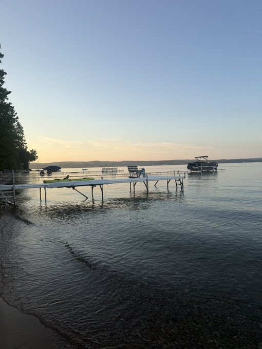 A tranquil lakeside scene at sunset shows docks extending into calm water with a pontoon boat and a covered slip in the distance.

The serene view of boats sitting idle at their moorings offers a stark contrast to the post's excitement about chasing 100x gains on every new blockchain launch — sometimes peace and stillness beat chasing the next hype cycle.