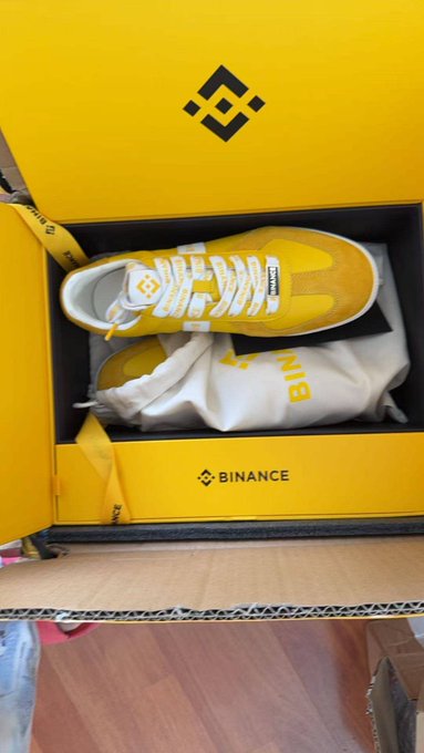 A pair of yellow and white Binance-branded sneakers displayed in a yellow Binance shoe box.