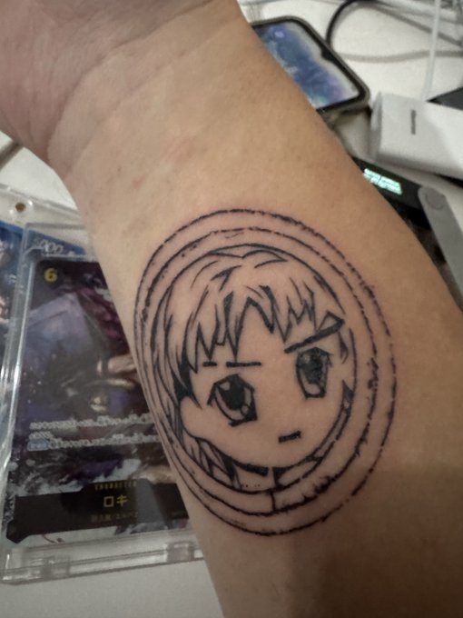 A tattoo of an anime-style character with short hair is inked on a person's forearm, displayed alongside a graded trading card slab (labeled "6") and a hardware wallet on the desk. The post celebrates a "rad" bull run, with the anime character's confident expression fitting the bullish sentiment and the visible collectibles—slabbed cards and crypto hardware storage—representing the "radbro" lifestyle of trading and investing.