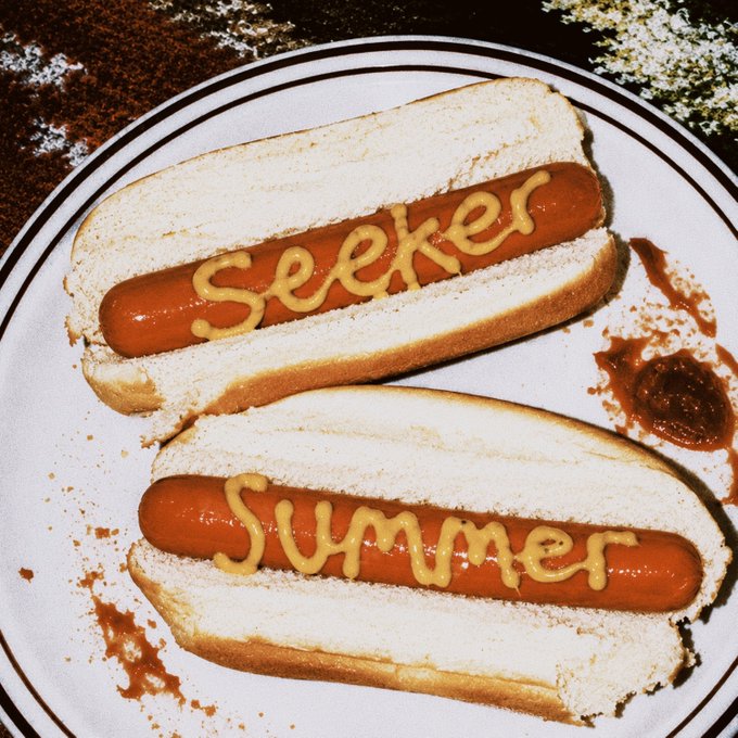 Two hot dogs on a white plate with mustard written on them reading "Seeker" and "Summer," a playful nod to the post's announcement about Seeker Summer Round 3 quests ending on August 12 at 2pm UTC.