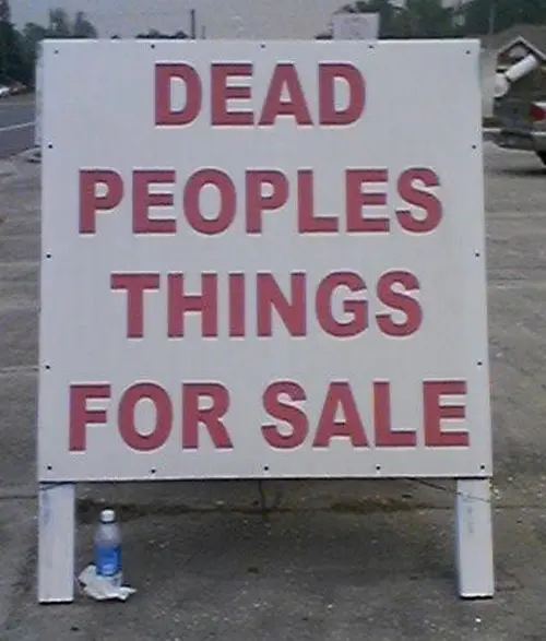 A roadside sign reads 'DEAD PEOPLES THINGS FOR SALE' in red letters on a white background, with a water bottle placed at its base.