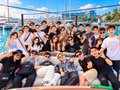 A group photo of smiling students posing together outdoors, making hand gestures like peace signs.