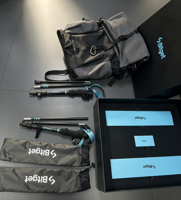 A collection of travel photography equipment is laid out on a dark surface, including a backpack, tripod, and carrying bags. The items and packaging feature the brand name 'Bitget' in light blue and white text.