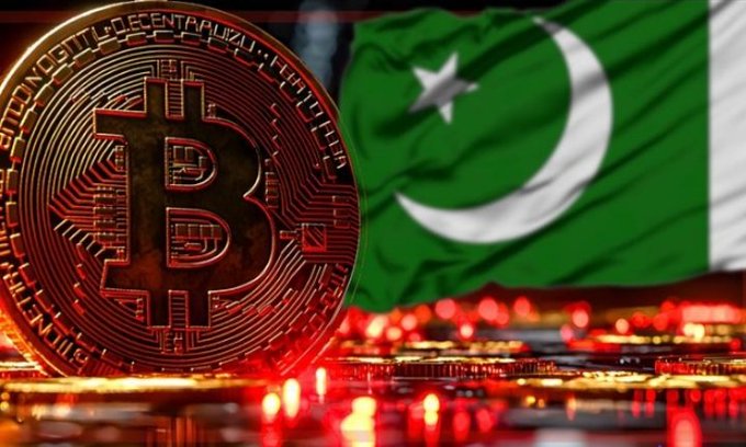A bronze Bitcoin coin stands upright against the backdrop of the Pakistani flag, with illuminated circuit board elements in the foreground.