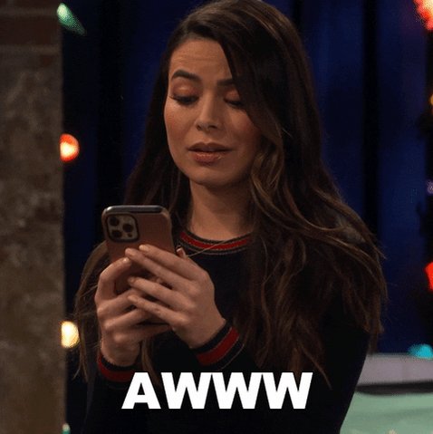 The image features a woman with long brown hair, who appears to be looking at her cell phone while standing near a blue wall. She seems to be reading or texting on her phone, possibly checking messages or browsing social media. The background of the image is filled with lights and colors, which adds to the overall atmosphere of the scene. The text "AWWW" can also be seen in the image, but it does not seem to have any direct connection to the woman using her cell phone.
