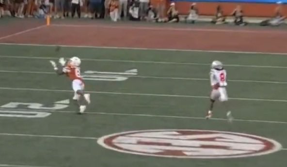 A football player wearing a Texas Longhorns jersey with the number 5 makes a catch or deflection on the field, while an opposing player wearing number 8 runs nearby. The image relates to the caption by capturing the moment leading to Arch Manning's interception in a Texas game.