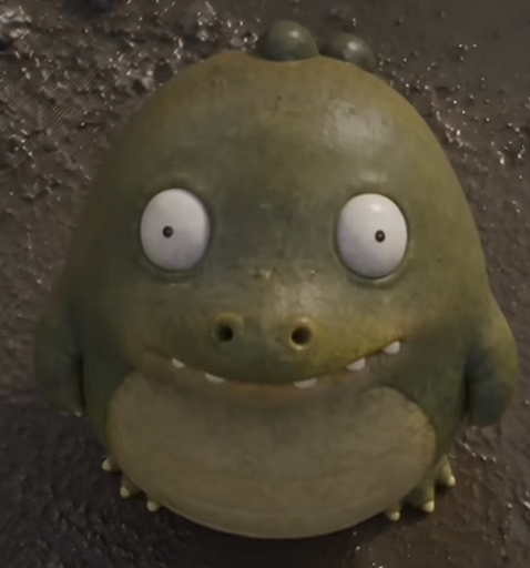 A chubby, green, wide-eyed monster figurine with a goofy grin and small horns sits against a dark, textured background, looking more comical than ferocious. The image appears alongside a post joking about this adorable creature aspiring to become a fierce beast after being unboxed, tied to the IP address "0x36e5cce1861ea0e7f2cb2b3472eb8d6350c97777."