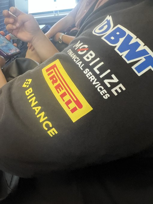 A close-up of someone wearing a black BMW jacket featuring Pirelli, Mobilize Financial Services, and Binance sponsorship logos.