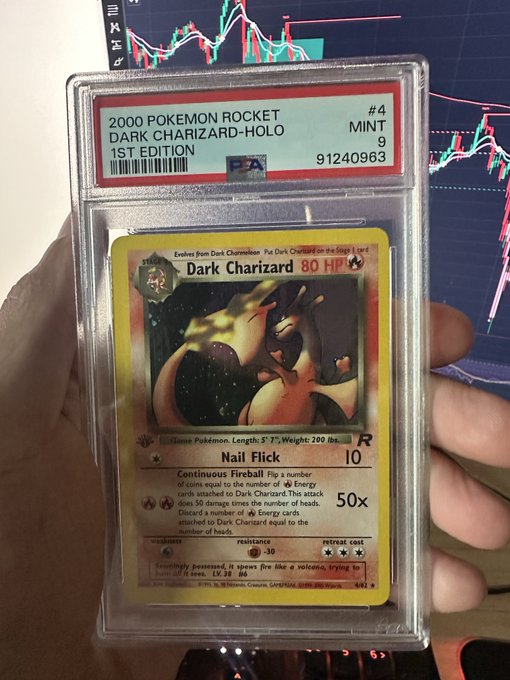 A hand holds a PSA-graded Mint 9 1st Edition holographic Dark Charizard #4 from the 2000 Pokémon Rocket set (cert #91240963), in front of a TV displaying a stock chart. The image relates to the post by showing the "nice piece of cardboard" the user acquired while being "sidelined" on $ANSEM, contrasting a tangible collectible with stock market trading.