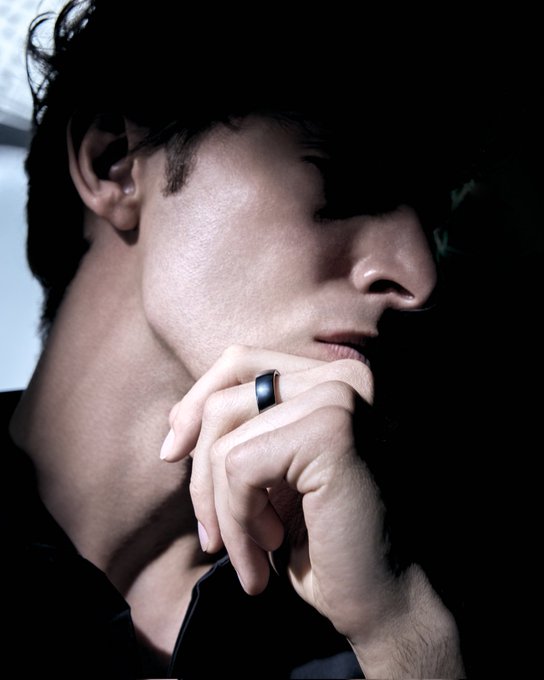 The image features a man wearing a black shirt, with his hand resting on his chin. He has a ring on his finger, which appears to be a unique piece of jewelry that serves as both an accessory and a functional wallet. The man's thoughtful expression suggests he is contemplating something or pondering the idea behind this innovative design.