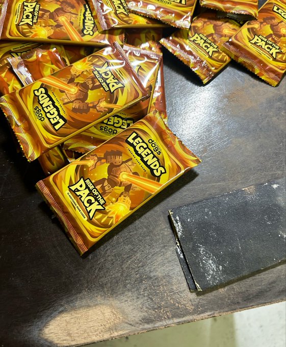 Several gold foil booster packs from 'Legends Rise of the Pack' trading card game are scattered on a dark surface next to a black foam insert.