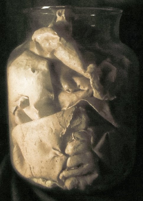 A glass jar filled with cracked, cream-colored stone or pottery fragments, illuminated dramatically against a black background.
