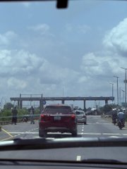 A dashcam view of a multi-lane highway on a sunny day with a red SUV driving ahead and overhead traffic sign gantries in the distance.