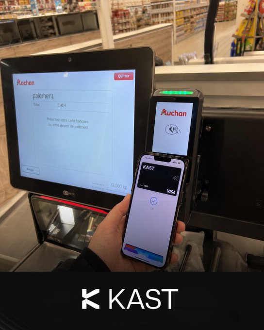 The image shows a person holding two cell phones next to a cash register. The person is using one of the phones to make a payment while the other phone displays an app called "@KAST" that seems to be related to cryptocurrency payments or transactions. This suggests that the individual might be exploring new ways to manage their finances and transactions, possibly opting for digital methods instead of traditional cash-based transactions. The image highlights the growing interest in modern technology and its impact on everyday life.