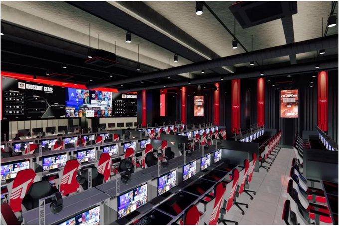 An interior view of a large gaming center with rows of gaming PCs, red and black chairs, and screens labeled 'GAMERS1 STAGE'.