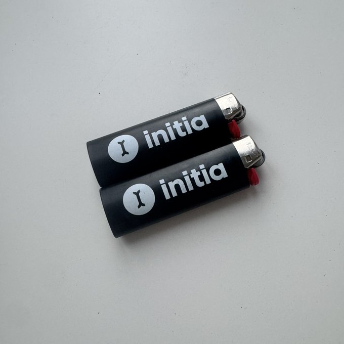 Two black disposable lighters sit on a white surface, both featuring the 'initia' logo with a circular icon.
