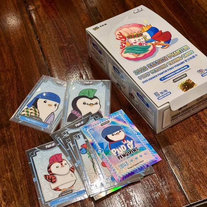 A 2025 Phantom Trading Cards box labeled 'LiLi PUDGY PENGUINS' sits on a wooden surface alongside several trading cards featuring cartoon penguins in various outfits.