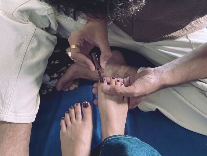 An overhead photo showing an adult clipping the toenails of a small child seated on their lap.