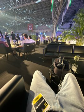 A person rests their legs (in jeans) on an airport terminal bench near gate 23, with a boarding pass tucked into their pocket and a backpack on the seat—readying for travel in what appears to be "MOONPAY MODE."