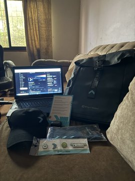 A casually arranged travel or work setup on a beige couch, featuring an open laptop displaying analytics, a black backpack, a black cap, and small product packets on the seat.