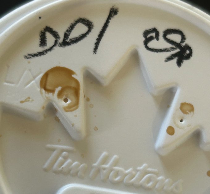 A close-up of a white Tim Hortons cup lid reveals the handwritten order '201' with coffee spilled across the surface.