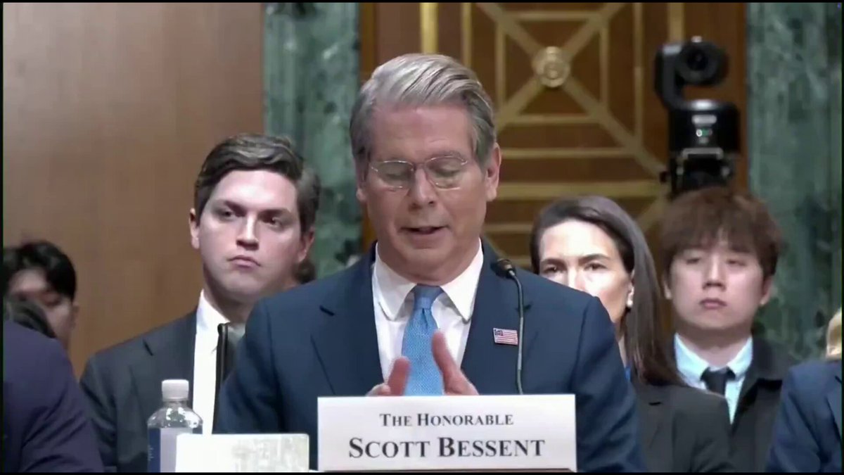 The image shows a man giving a speech at a press conference while standing behind a podium. The man appears to be dressed in a suit, with glasses on his face. He is speaking into a microphone, which can be seen clearly against the background of the room where he is addressing an audience. The text "Scott Bessent: We are moving forward with all deliberate speed on the Strategic Bitcoin Reserve." suggests that the man is discussing the development and implementation of the Strategic Bitcoin Reserve, which is a digital asset management system designed to store and manage Bitcoins securely.
