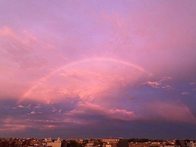 A pink and purple sunset sky over a cityscape, featuring a rainbow arcing across the clouds.