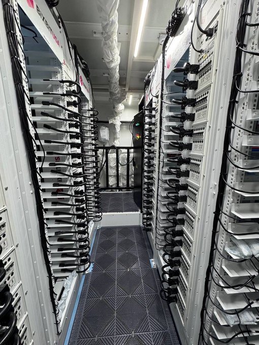 A photo looking down an aisle of server racks filled with networking equipment and extensive black cabling.
