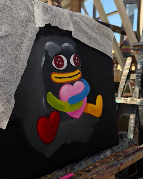 The image features a black canvas with a colorful cartoon penguin holding a heart, surrounded by various other hearts of different colors. The penguin appears to be smiling, giving off a cheerful vibe. In the background, there are two people standing next to each other and another person sitting on a chair. The post also includes text that reads "Gm $TON Process #NFTCommunity".