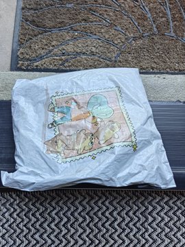 A crumpled white shirt or fabric lies on a textured mat and concrete surface, featuring a printed image of cleaning supplies including a spray bottle, brush, and bucket.