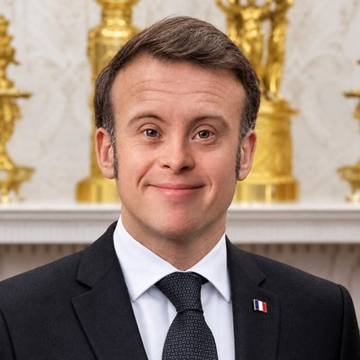 An official portrait photograph of Emmanuel Macron wearing a dark suit with a French flag pin, smiling slightly, taken in what appears to be an ornate official room with gilded decorations.